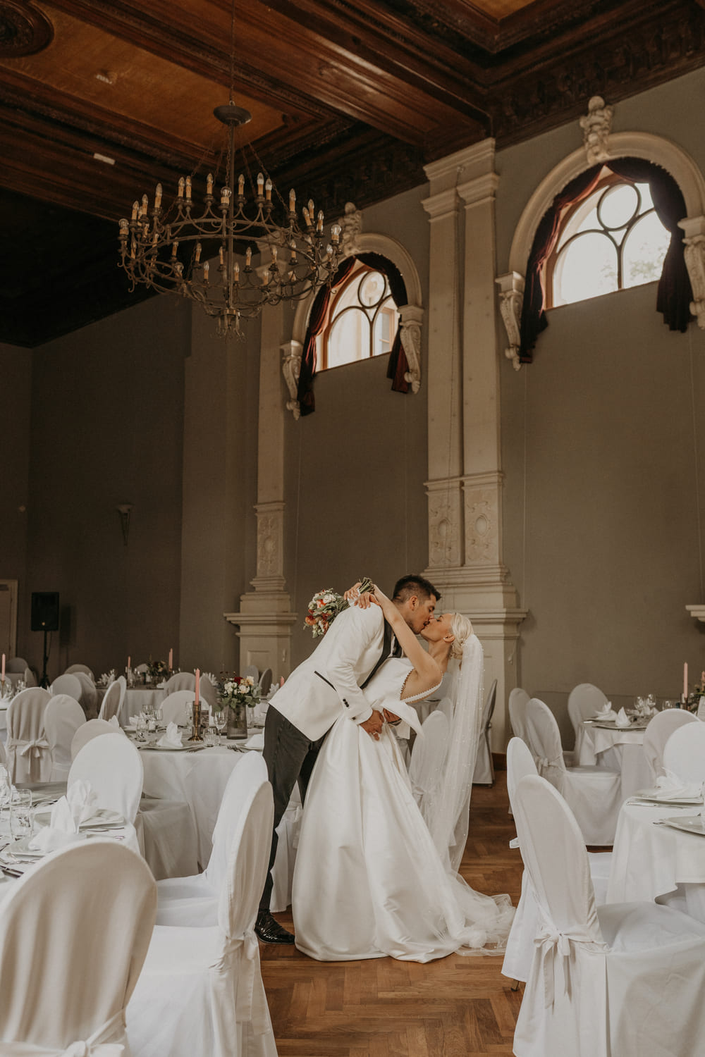 Brautpaar küsst sich und im Hintergrund wird der eingedeckte Saal gezeigt