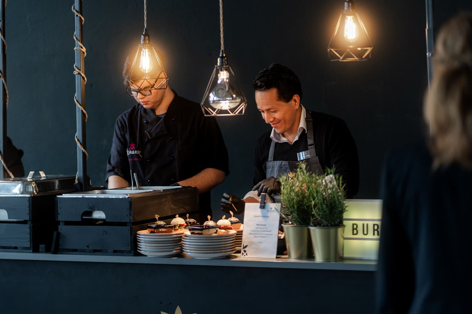 Schuler Service und Koch stehen hinter der Theke und richten Speisen an